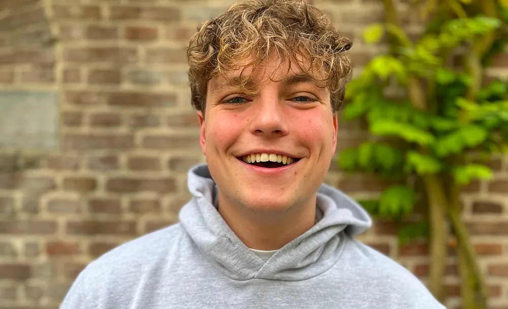 Lachende jonge StudyWorker in grijze hoodie voor een bakstenen muur