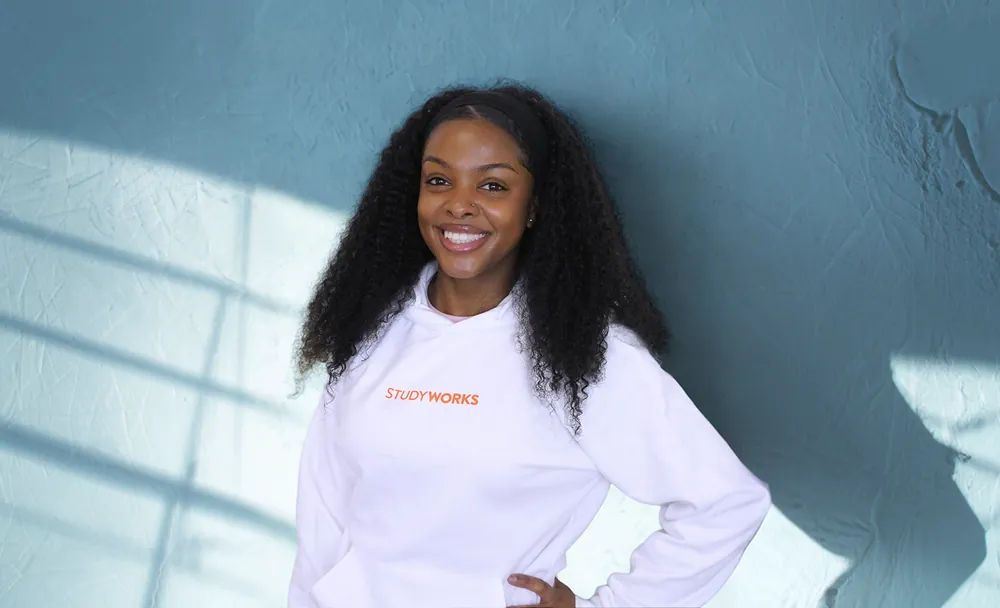 StudyWorker in witte StudyWorks-hoodie voor een blauwe muur