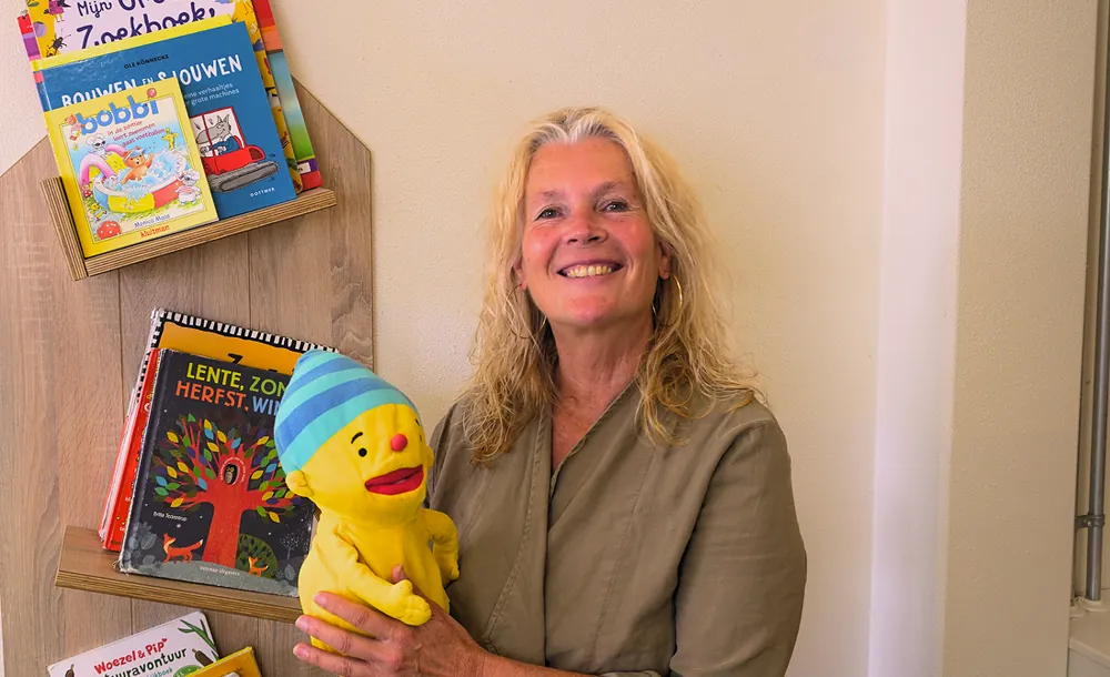 Pedagogisch medewerker met een handpop naast een kast met prentenboeken