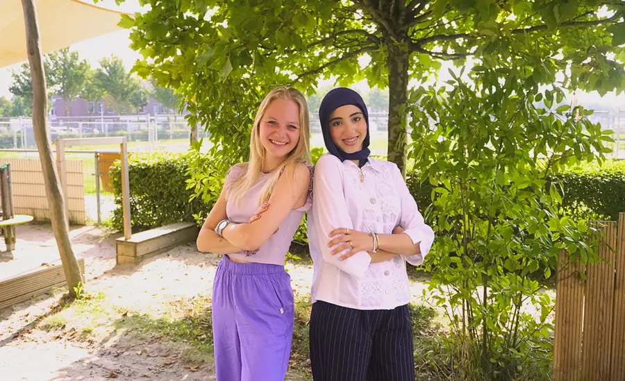 Twee collega's staan rug aan rug in de tuin van een kinderdagverblijf